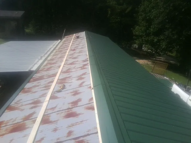 Old rusted panels beside newly installed green metal roofing — Wind Damage Roof Repair by Roofing Brothers in Wellsburg